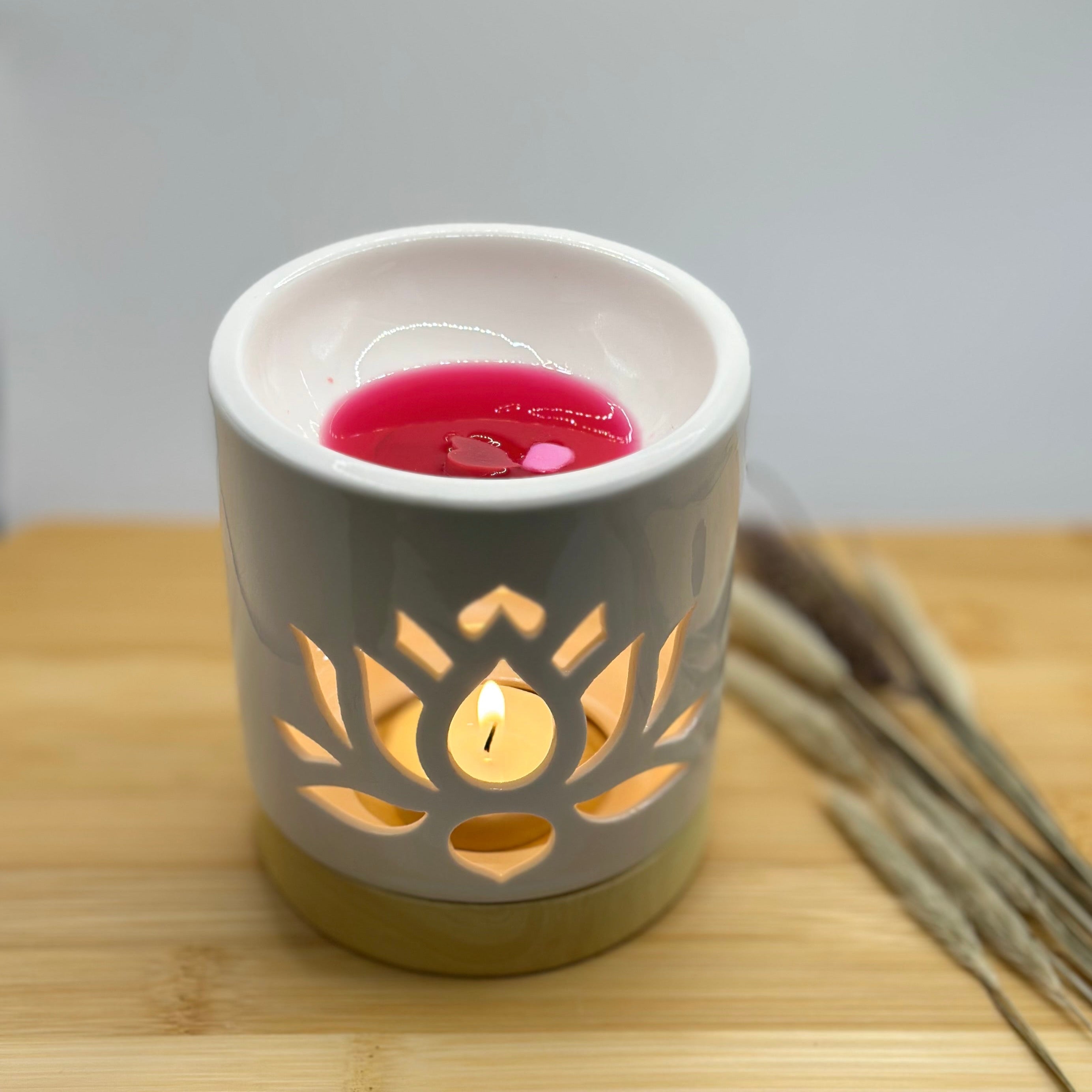 Brandende waxbrander met lotusbloem patroon in wit keramiek, wax melt in het schaaltje en theelicht zichtbaar door de uitsnede
