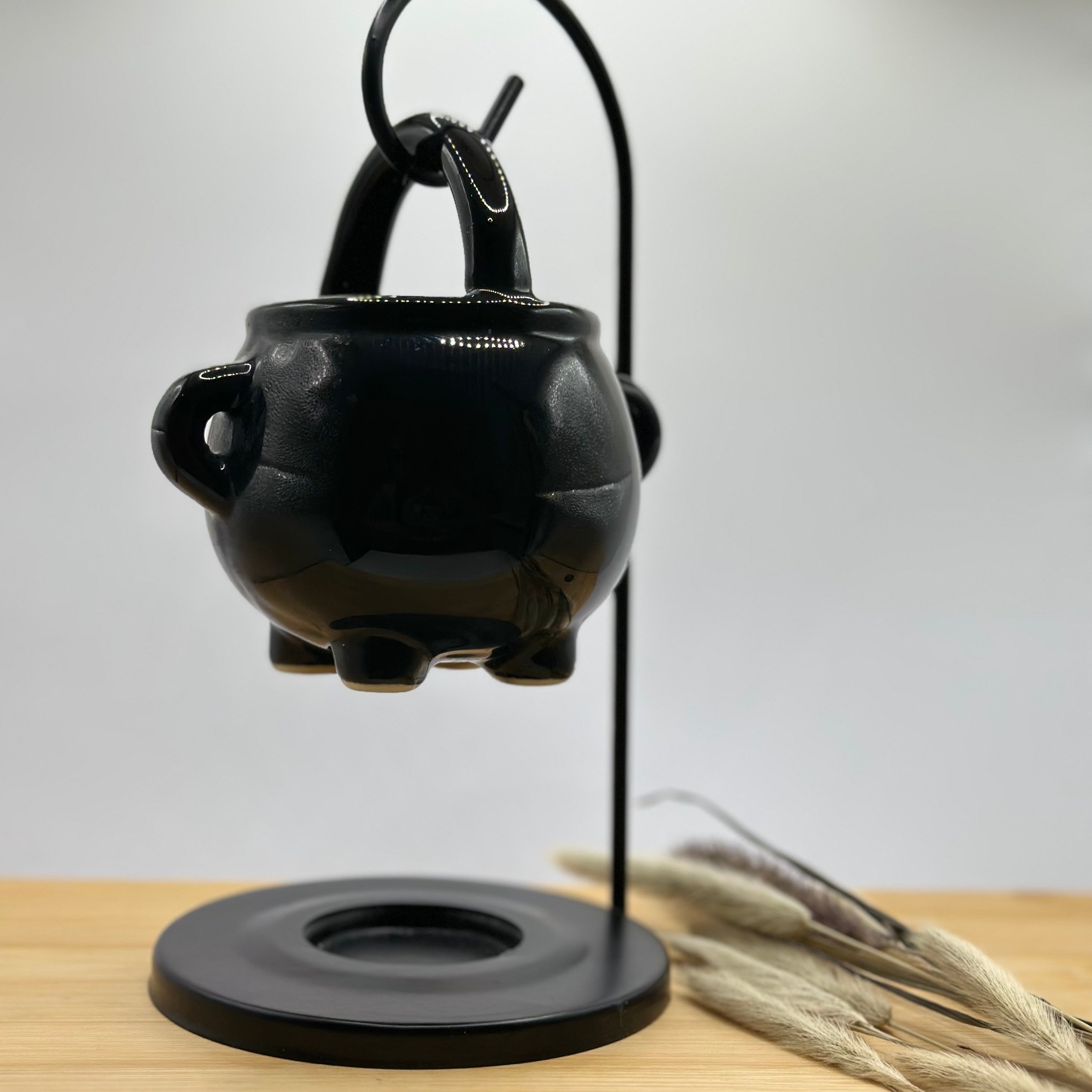 Detail van zwarte keramieken ketel waxbrander met oortjes en metalen standaard, minimalistische zwarte uitvoering.