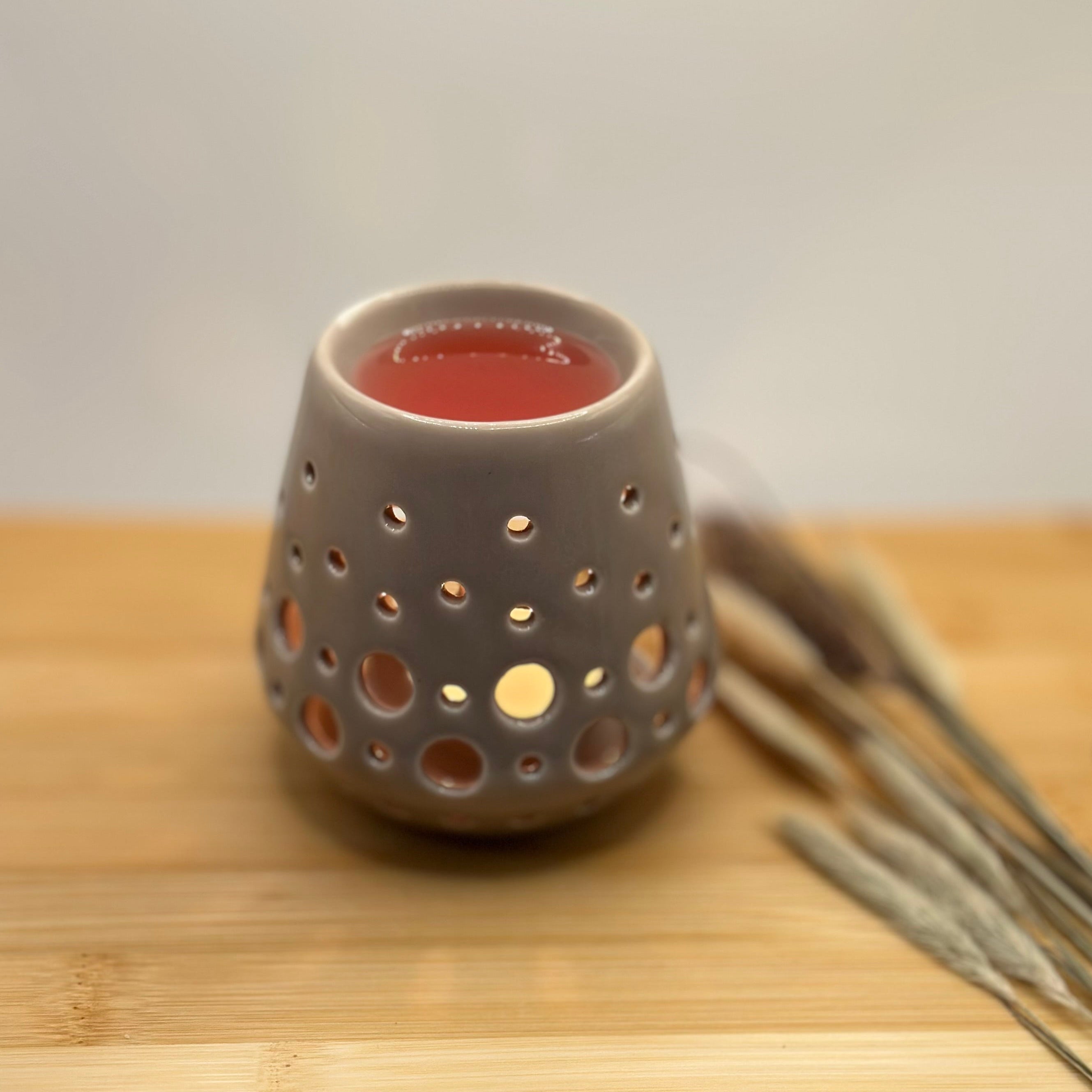 Grijze waxbrander met brandend waxinelichtje en gesmolten roze wax bovenin.