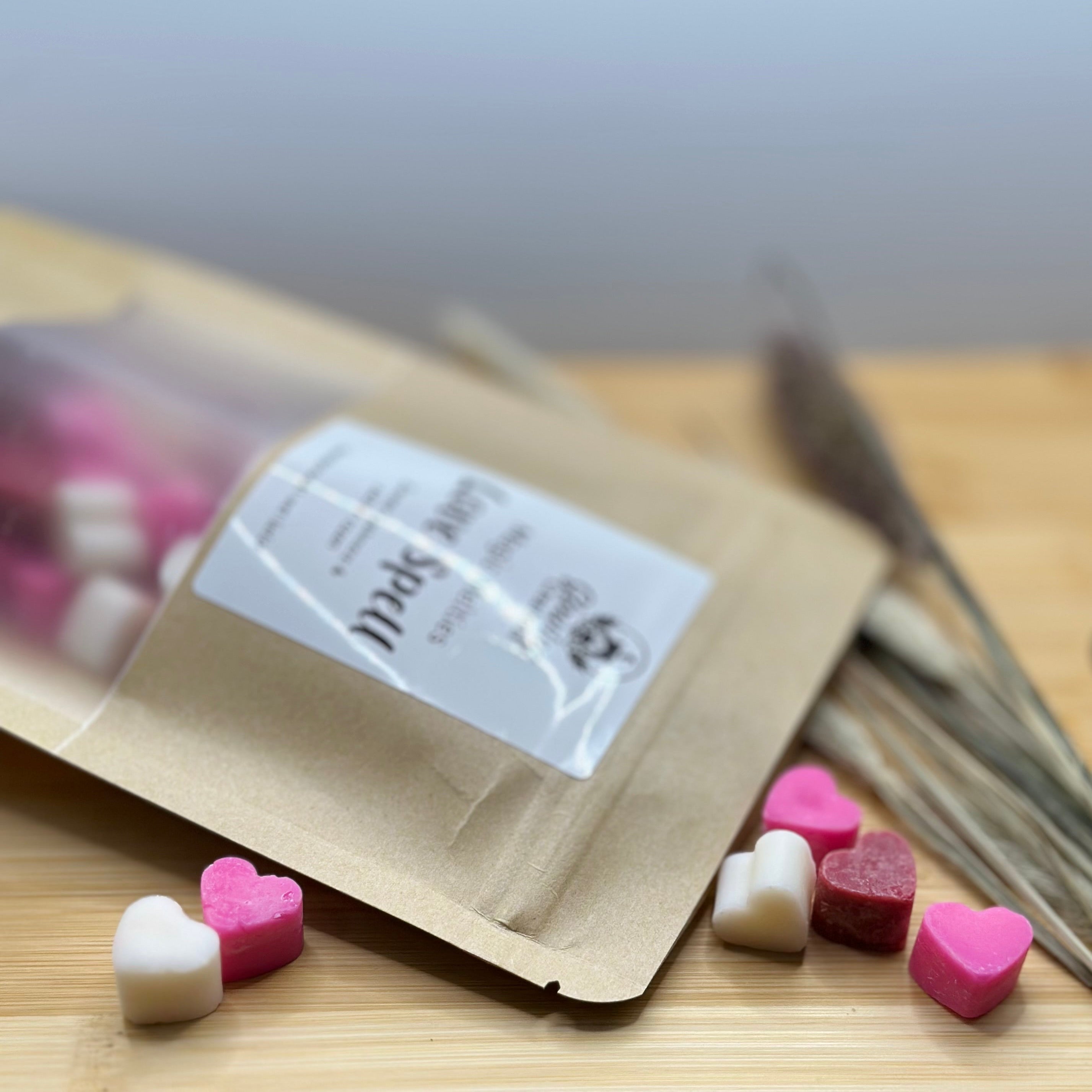Hartvormige wax melts Love Spell in roze, wit en rood met cashmere en rozengeur naast kraft zakje