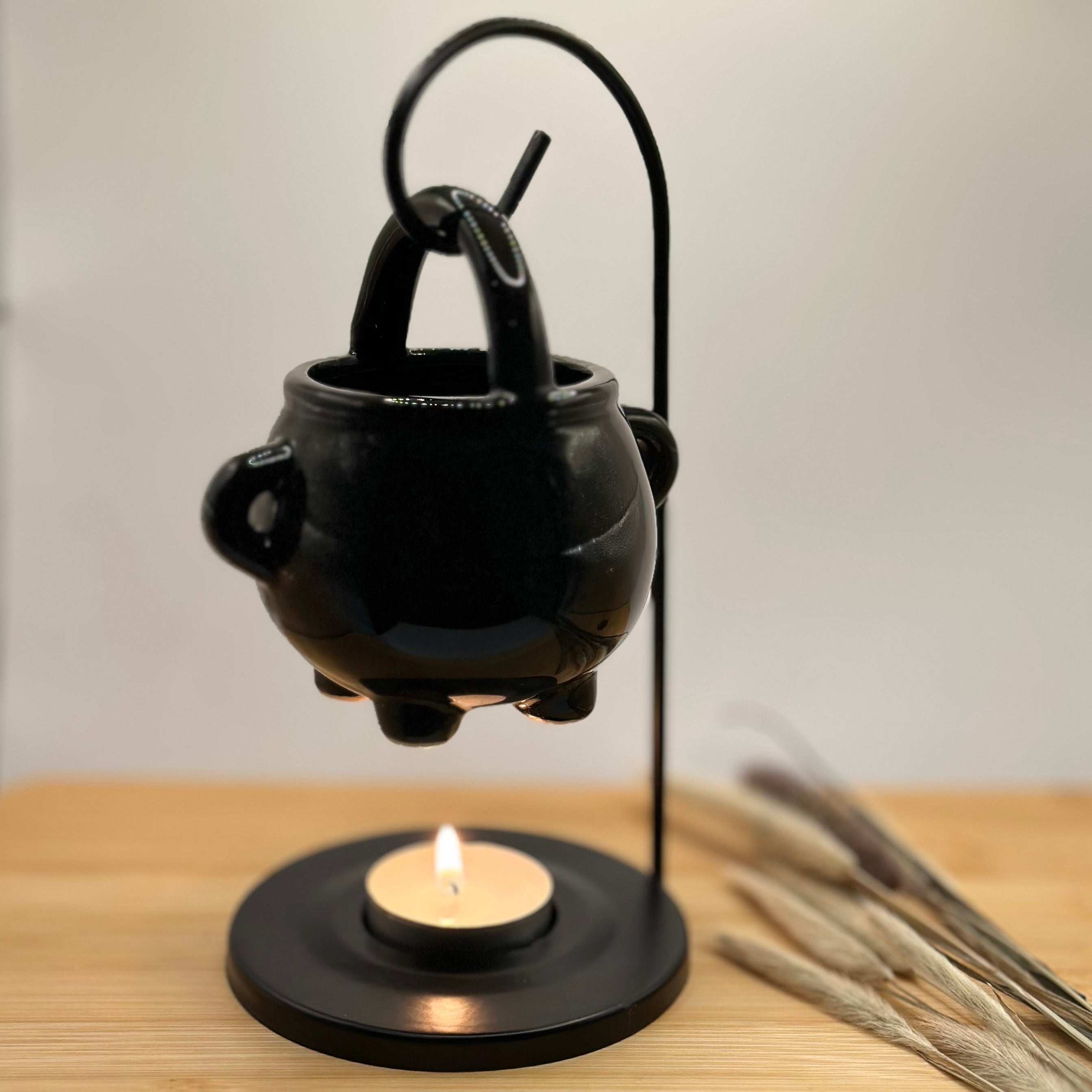 Zwarte keramieken ketel waxbrander met brandend waxinelichtje in metalen houder, sfeervol warm licht.