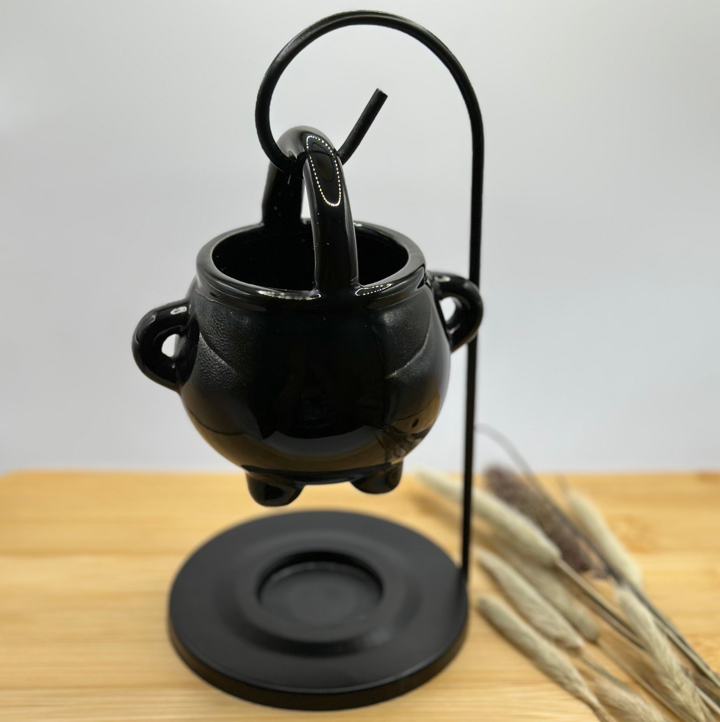 Zwarte keramieken waxbrander in de vorm van een ketel, hangend aan een zwarte metalen houder op ronde voet.